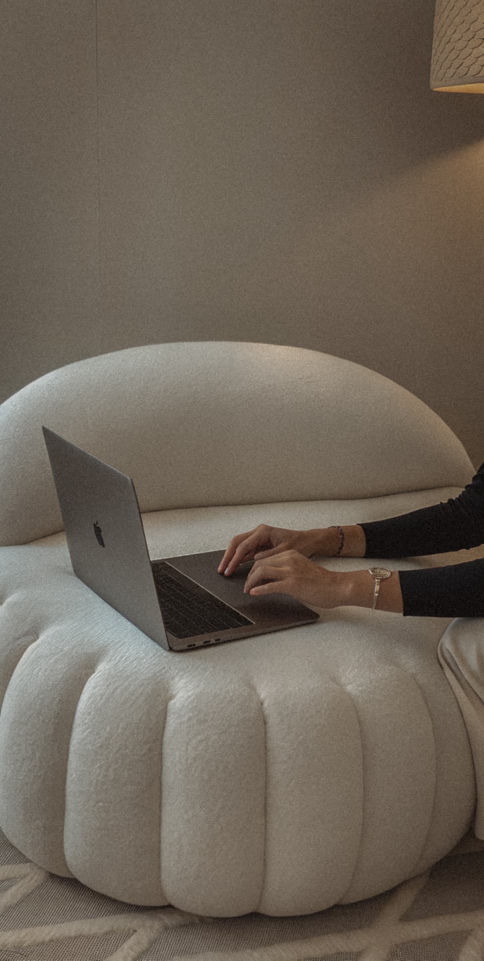 A woman working on a laptop while sitting on a cream boucle sofa