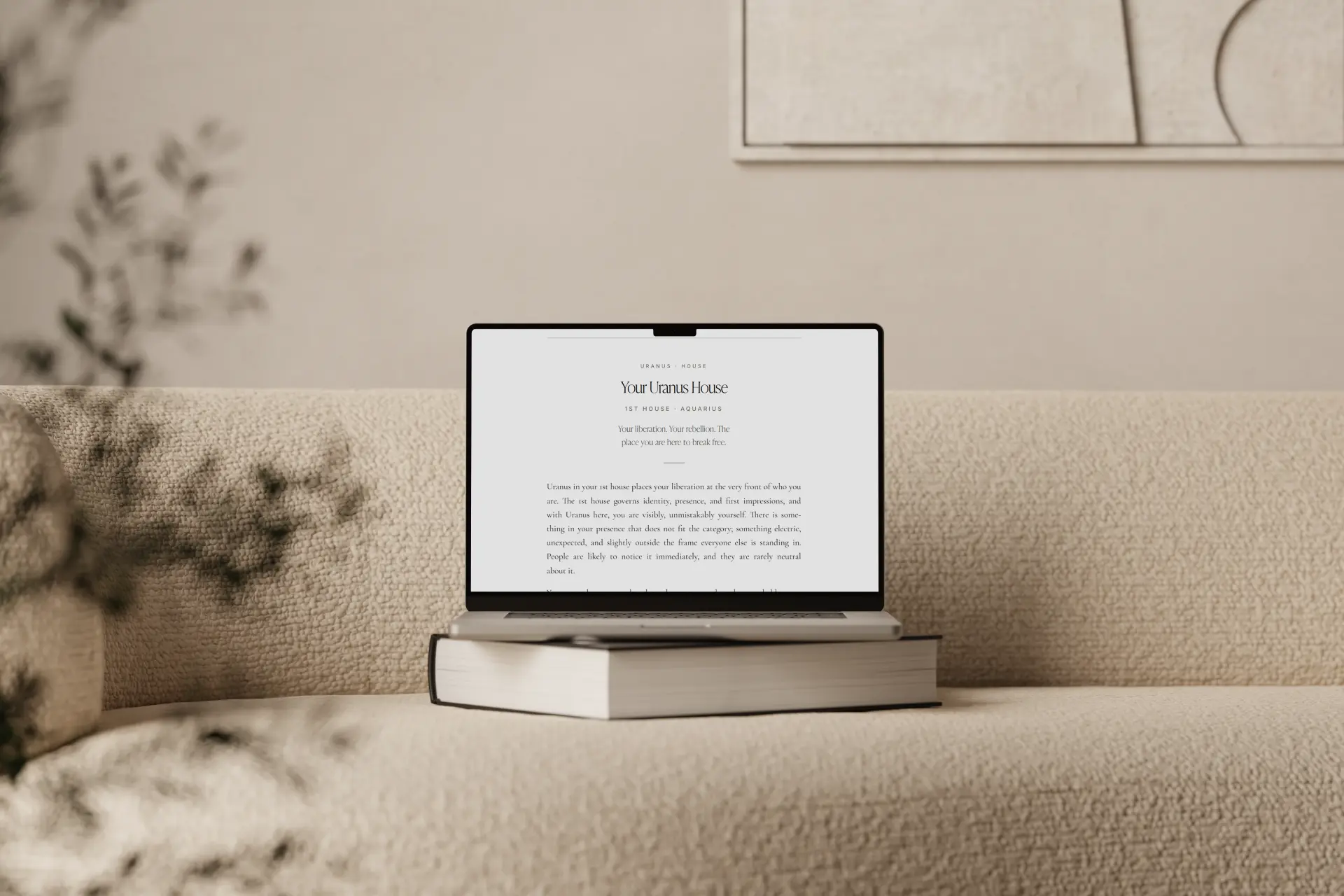 The Astrology Guide on a laptop resting on a book on a cream bouclé sofa, showing Your Uranus House